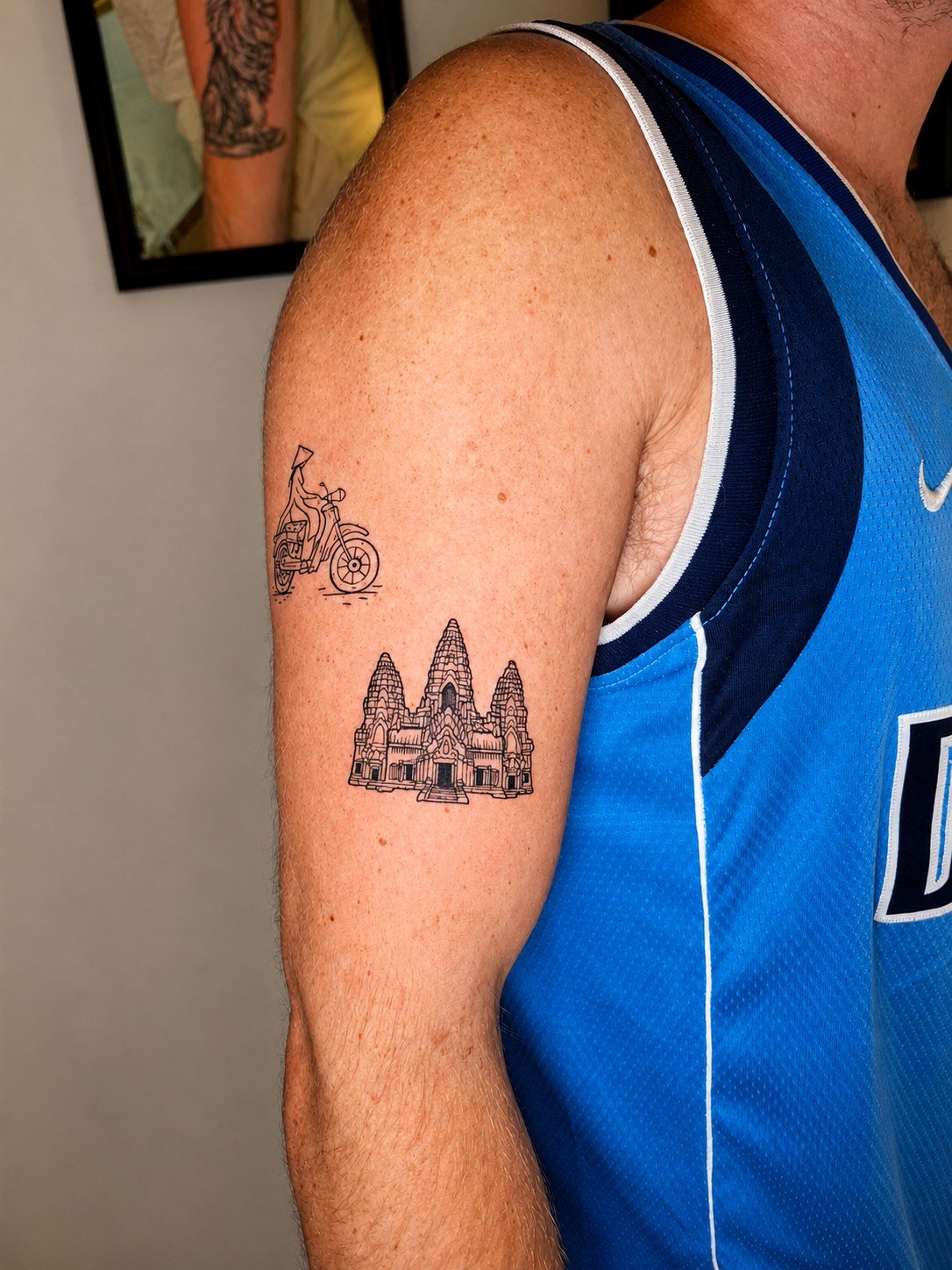 Detailed Angkor Wat towers and architecture in black linework on the upper arm, beneath a small motorbike tattoo. Tattoo by Edboi