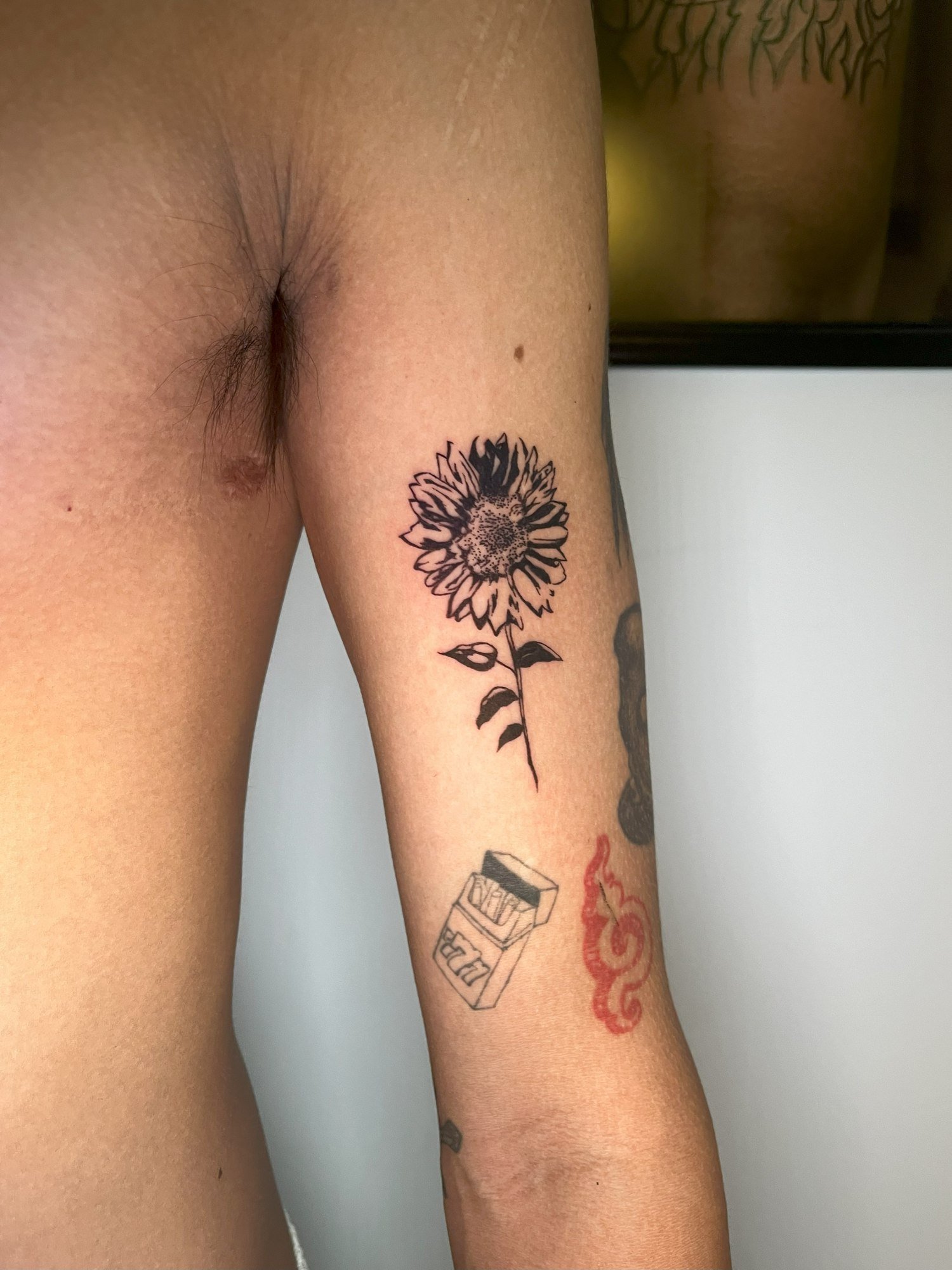 A sunflower with bold black petals, a dotted centre and leafy stem on the upper arm. Tattoo by Edboi