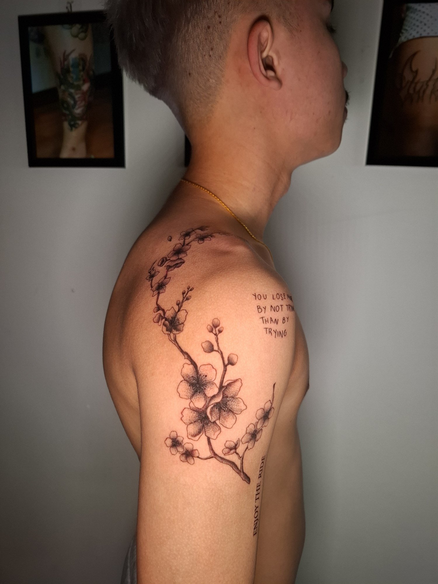 A flowering branch with delicate blossoms and buds following the shoulder and upper arm. Tattoo by Edboi