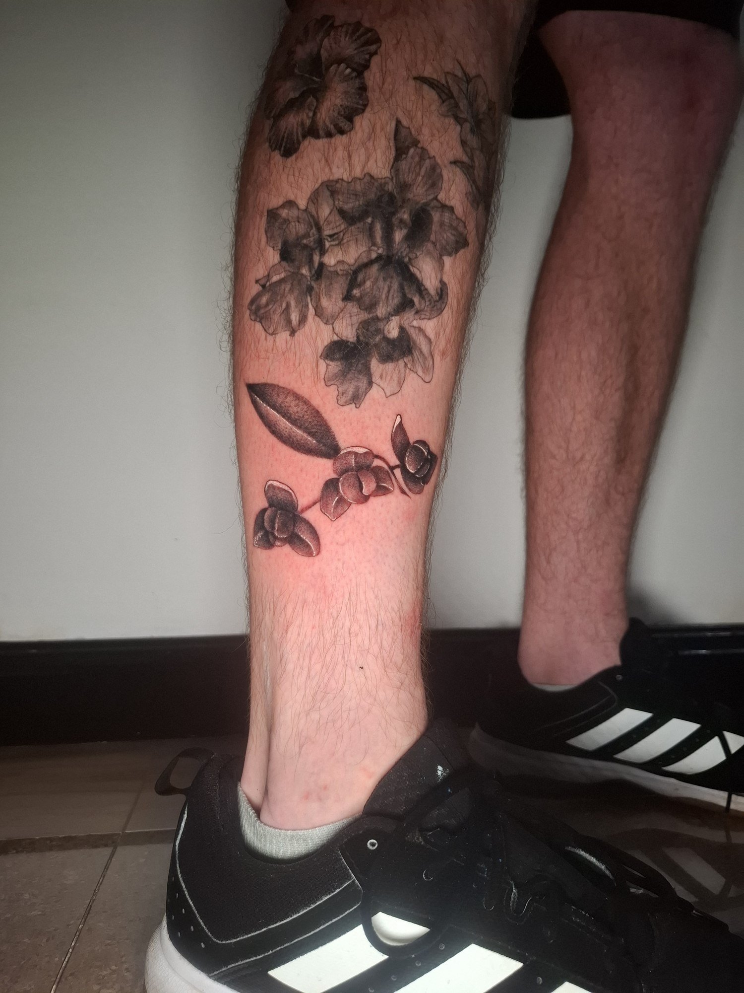 Shaded flowers and a leafy botanical sprig on the calf. Tattoo by Edboi