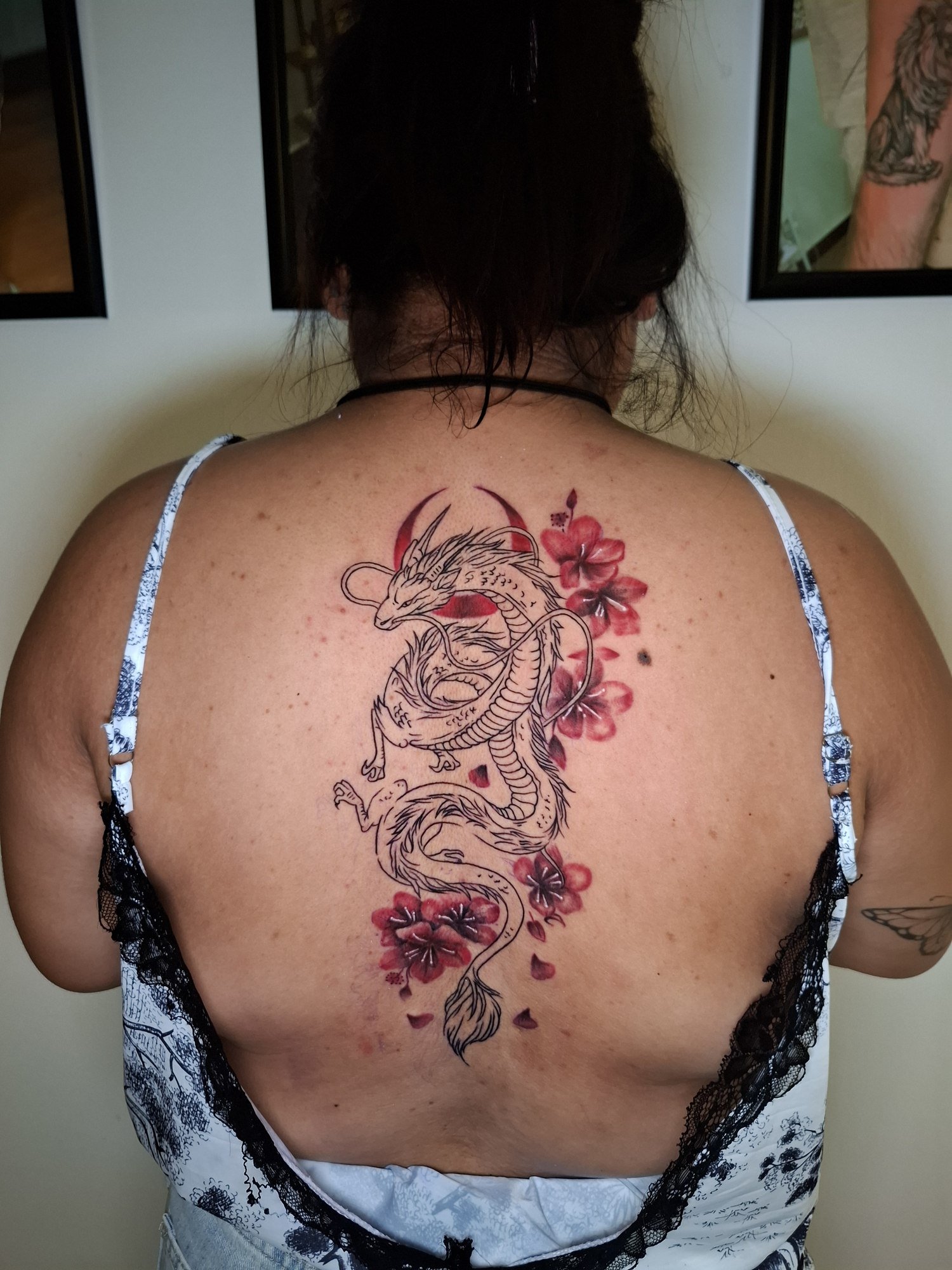A large winding dragon in black linework with red blossoms and a red crescent on the back. Tattoo by Edboi