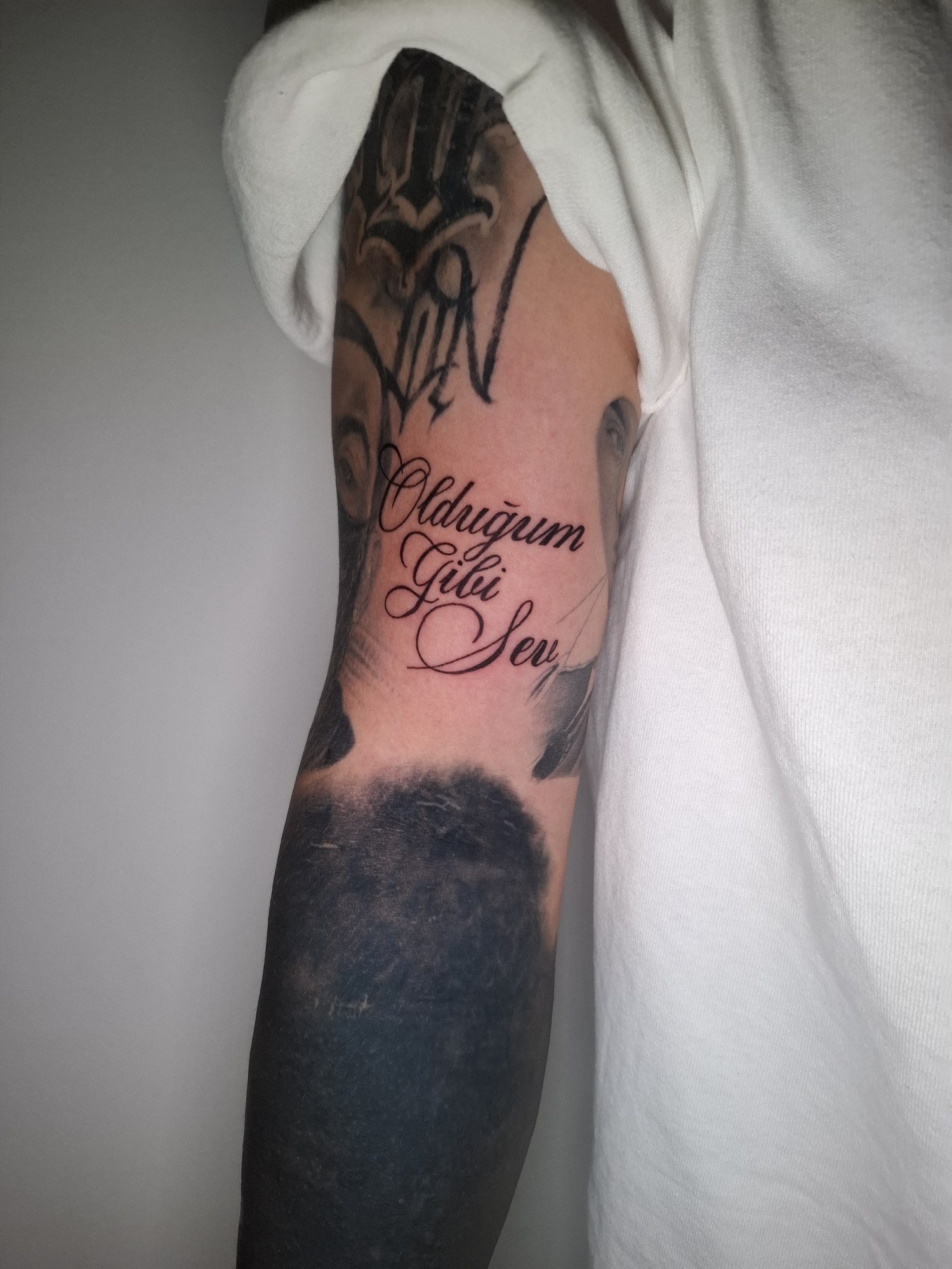 Three lines of black cursive lettering with long decorative flourishes on the inner upper arm. Tattoo by Edboi