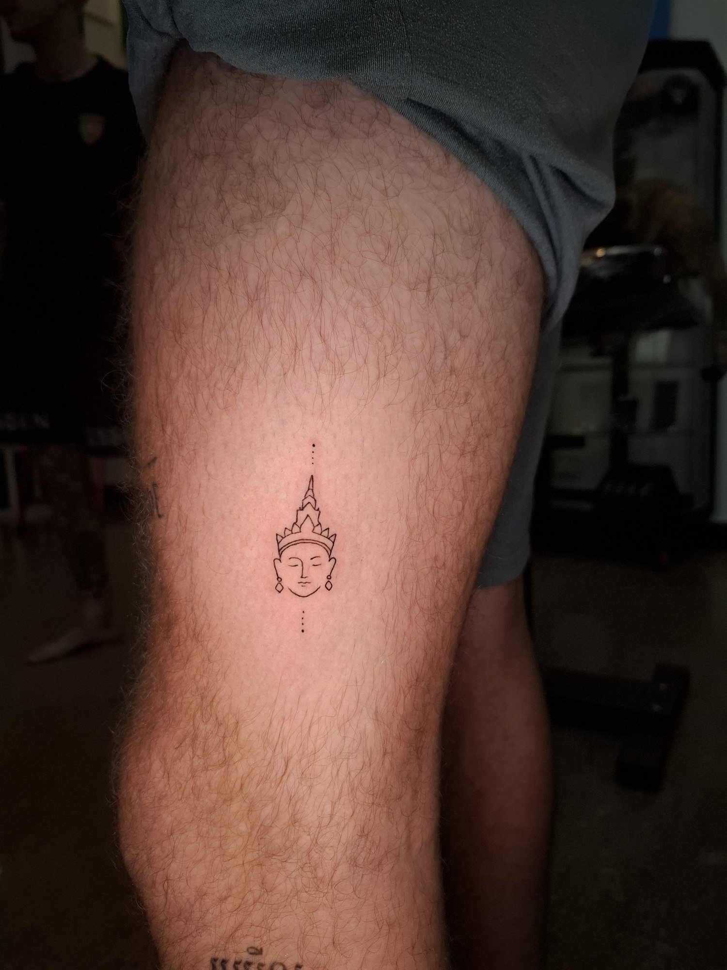A small outlined face with a pointed headdress on the leg. Tattoo by Edboi