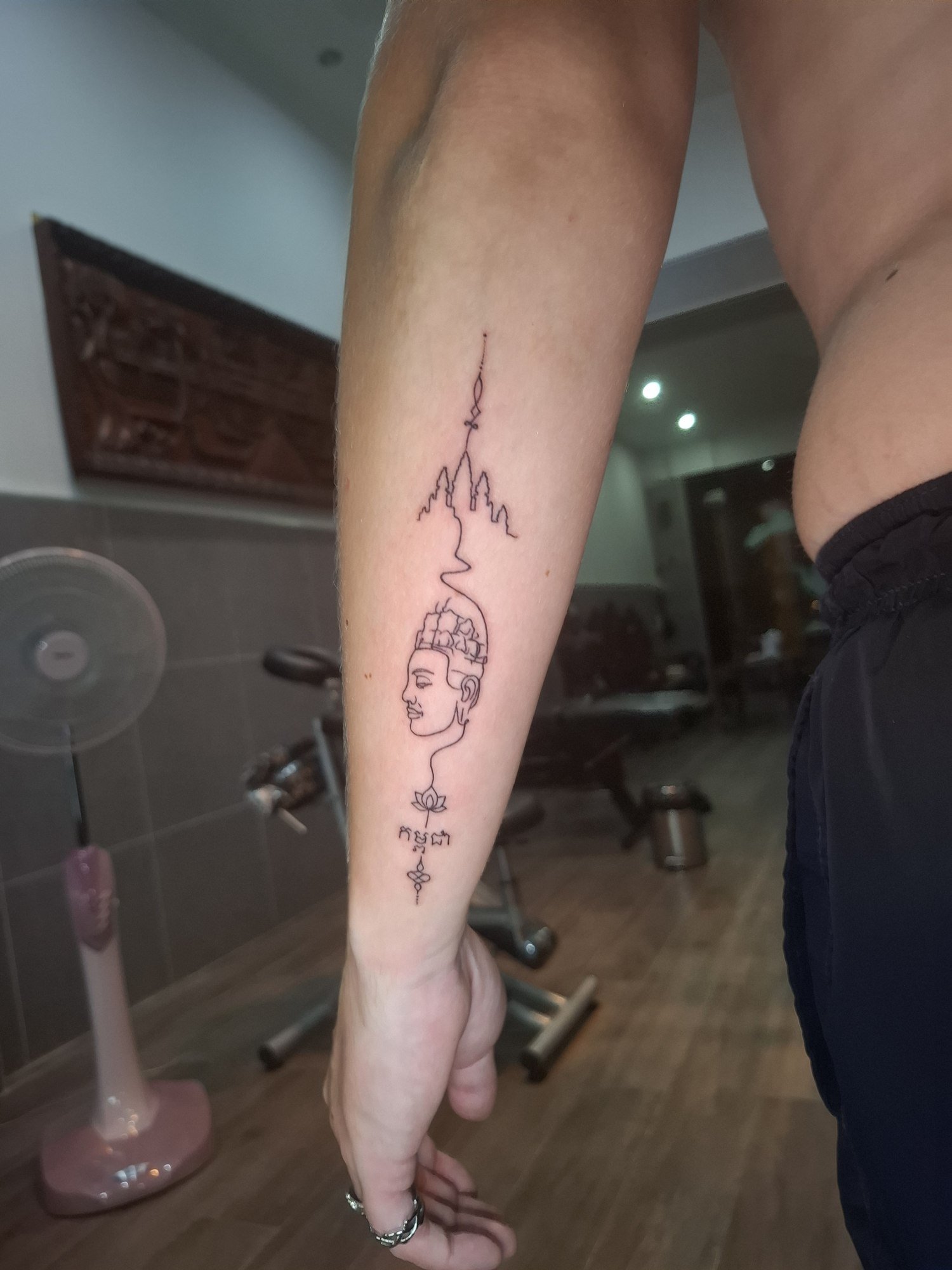 A fine outlined face between elongated ornamental symbols on the forearm. Tattoo by Edboi