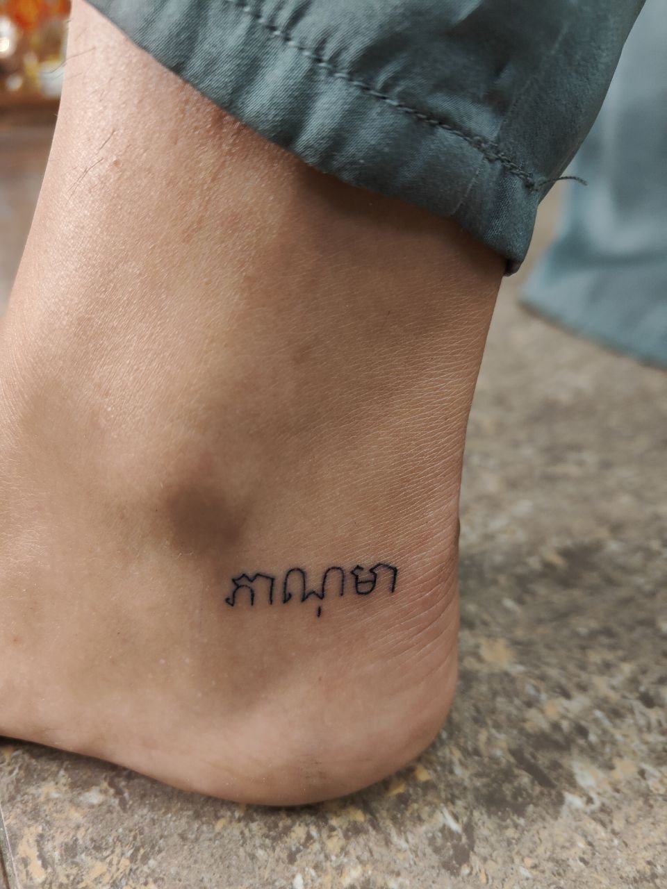 A short line of delicate Khmer lettering beside the ankle. Tattoo by Edboi