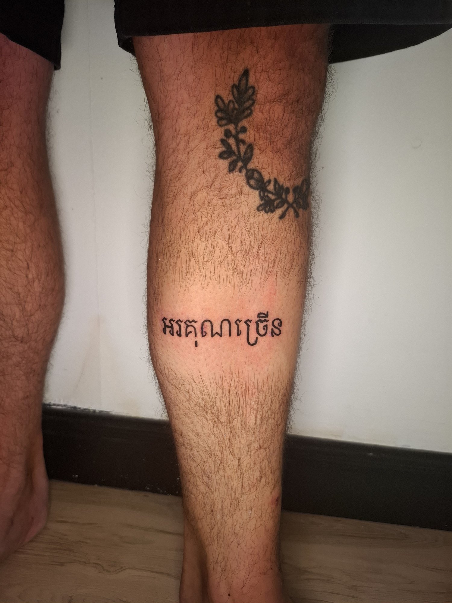 A horizontal line of black Khmer lettering on the calf. Tattoo by Edboi