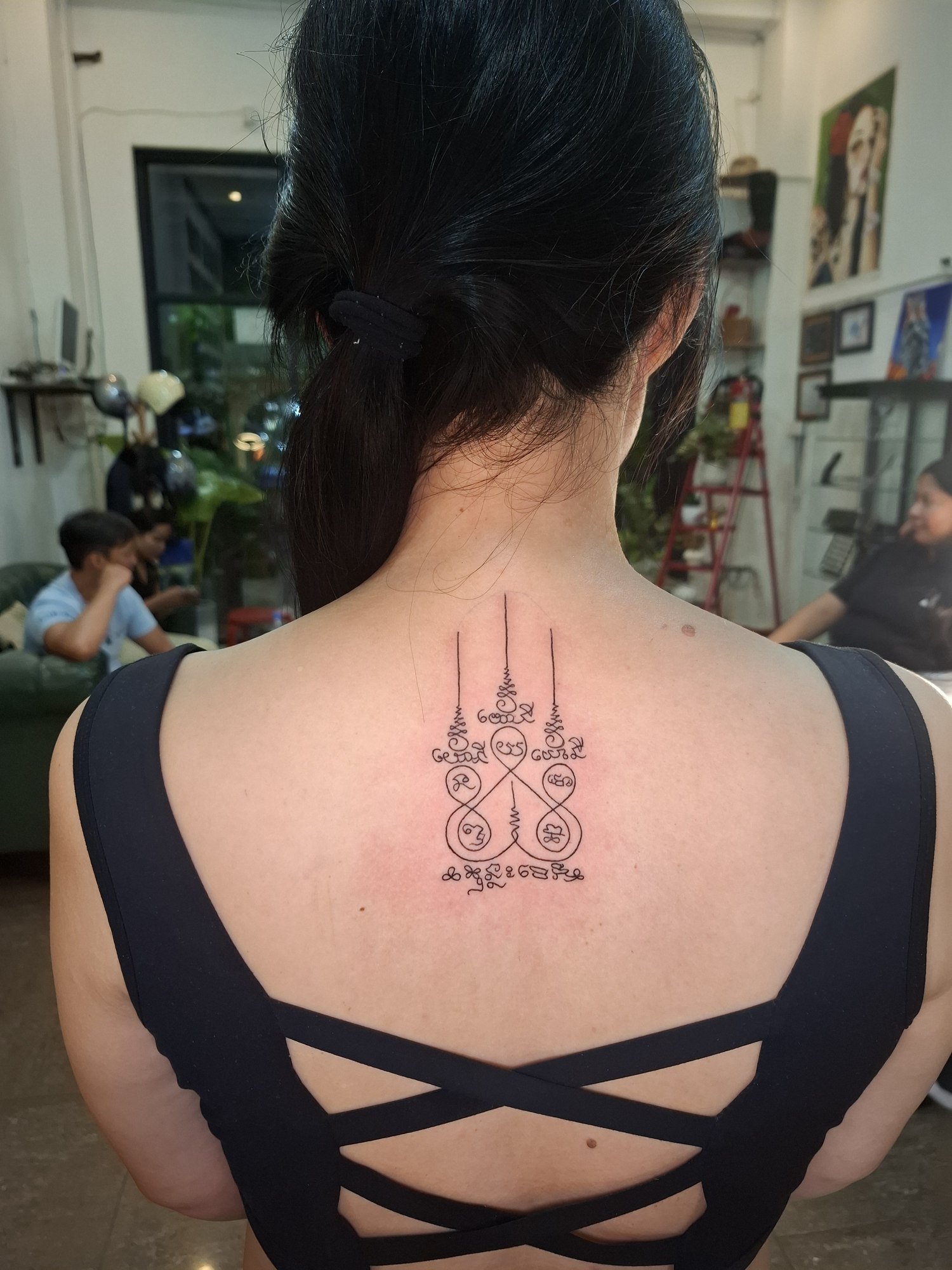 A symmetrical composition of looping symbols, vertical lines and ornamental script on the upper back. Tattoo by Edboi