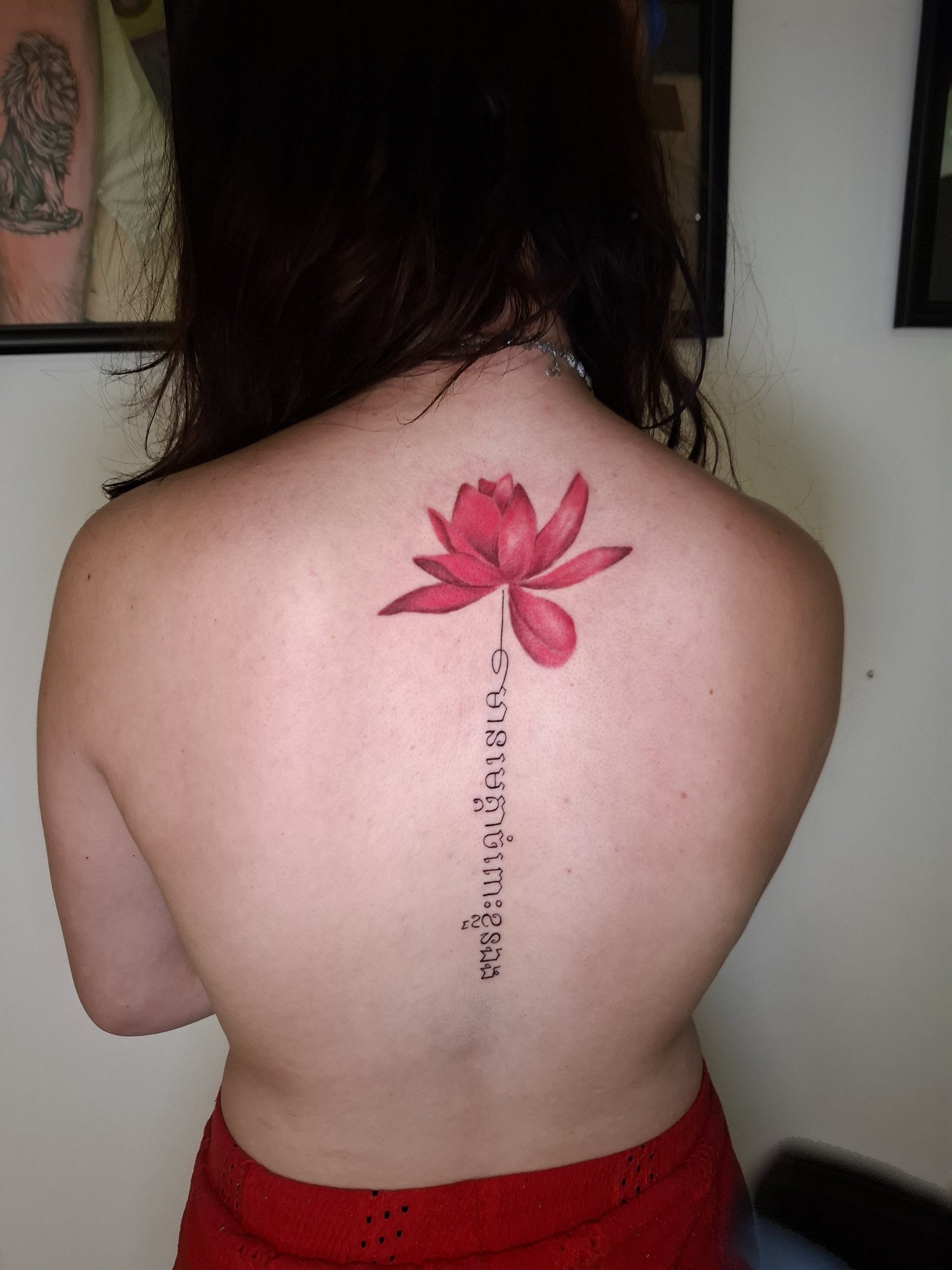 A pink lotus above a vertical line of Khmer lettering down the upper back. Tattoo by Edboi