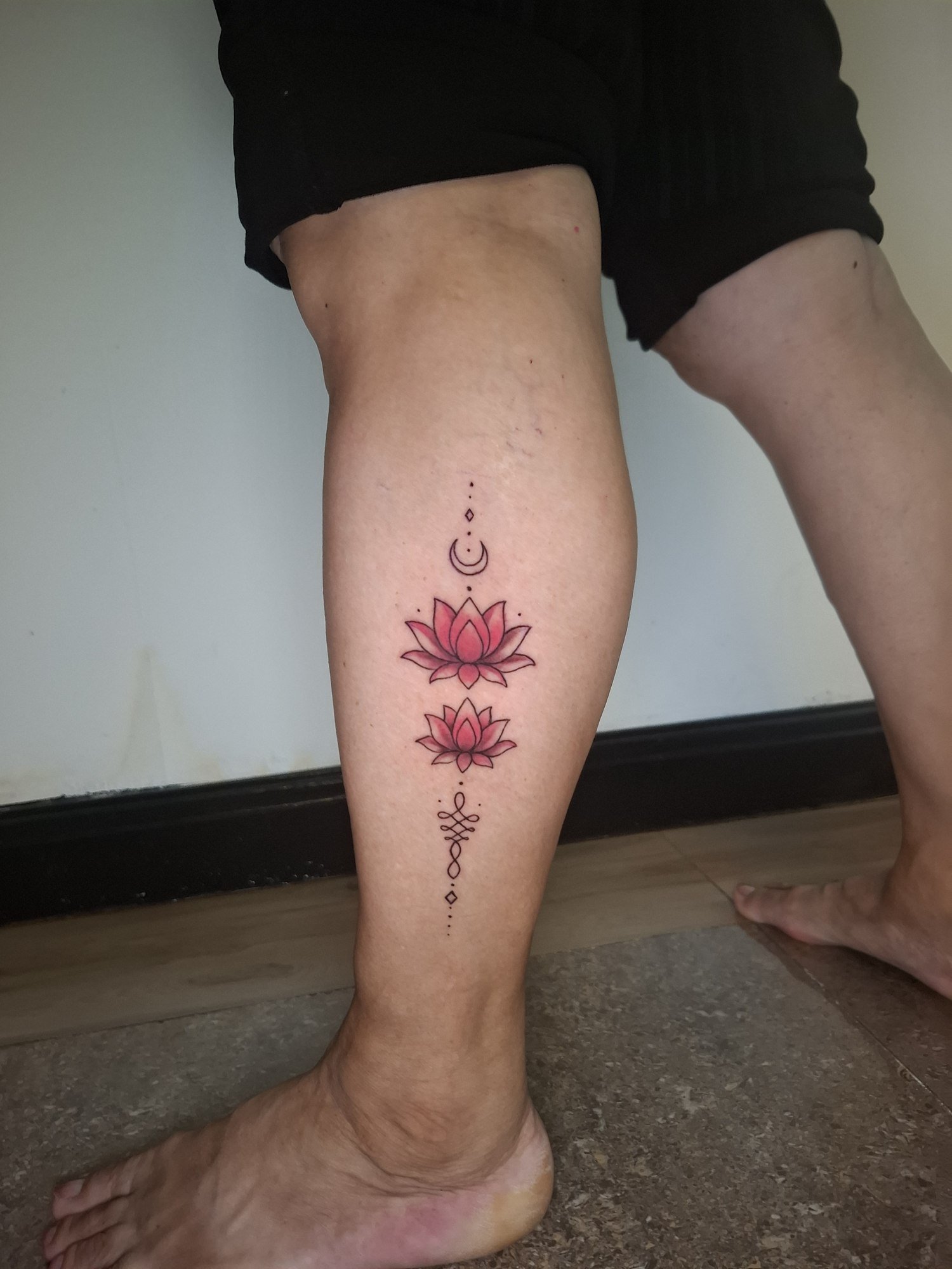 Two pink lotus flowers with a crescent moon, fine ornamental details and an unalome on the calf. Tattoo by Edboi