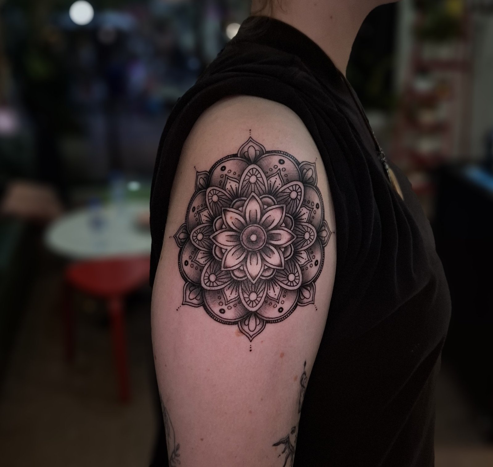 An intricate circular mandala with shaded petals and dotted details on the shoulder. Tattoo by Edboi