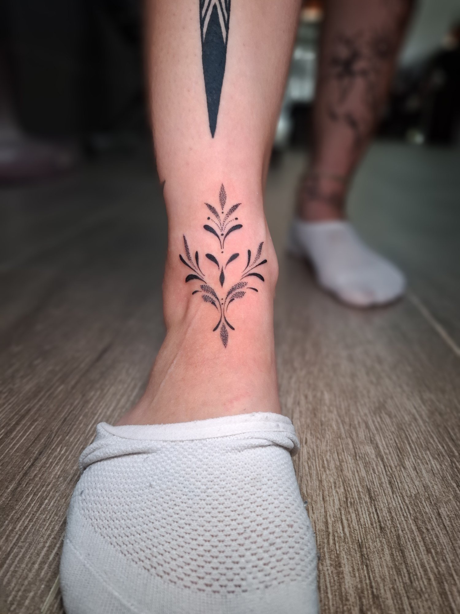 A symmetrical leafy black ornament above the ankle. Tattoo by Edboi