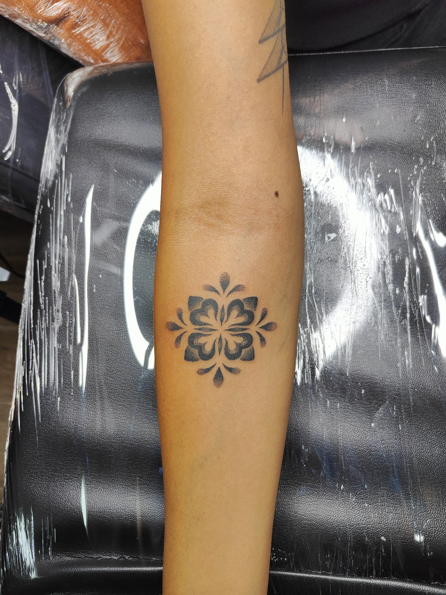 A small circular black floral mandala on the forearm. Tattoo by Edboi