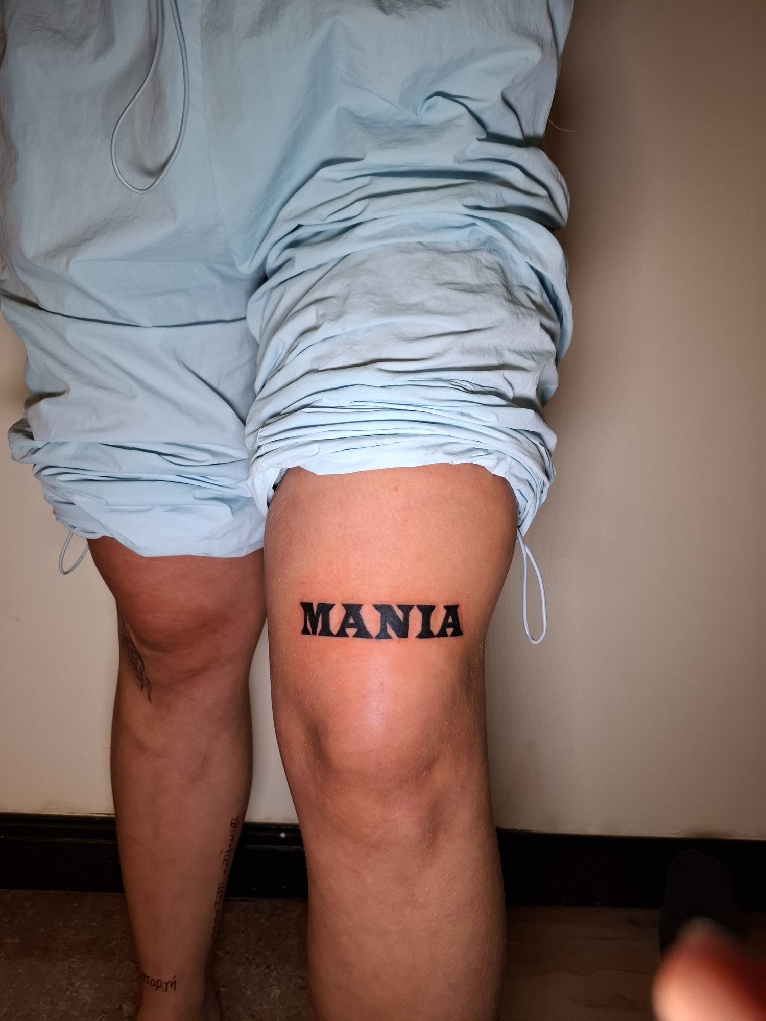 Bold black MANIA lettering above the knee. Tattoo by Edboi