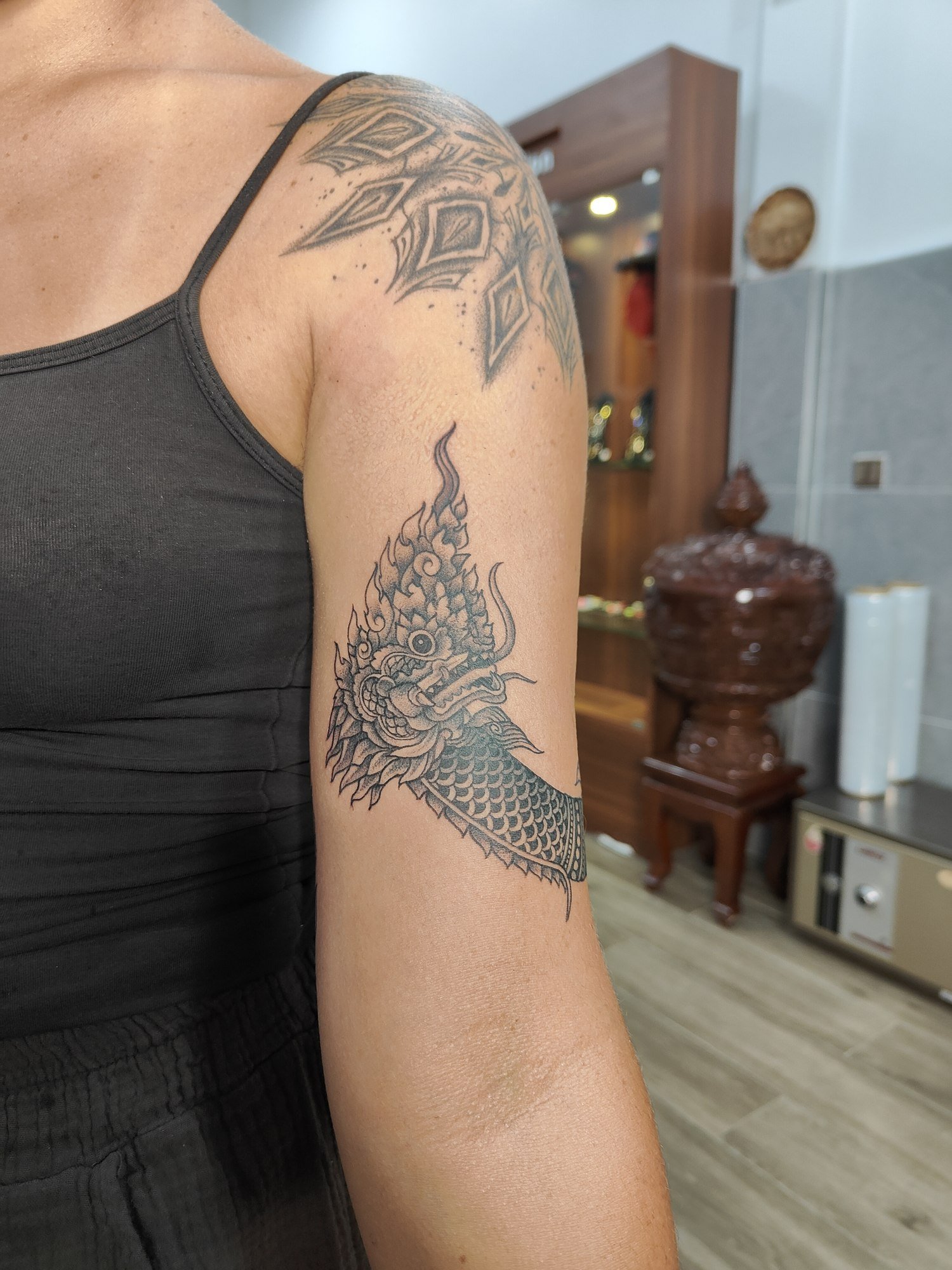 An ornamental Naga with detailed scales and a flame-shaped crest curving around the upper arm. Tattoo by Edboi