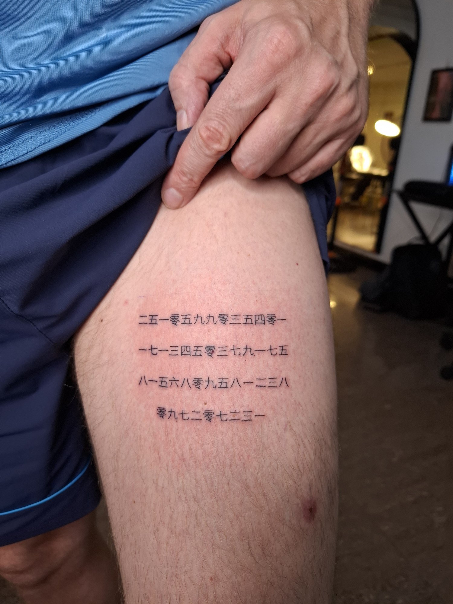 Four horizontal lines of small black numeral characters on the thigh. Tattoo by Edboi