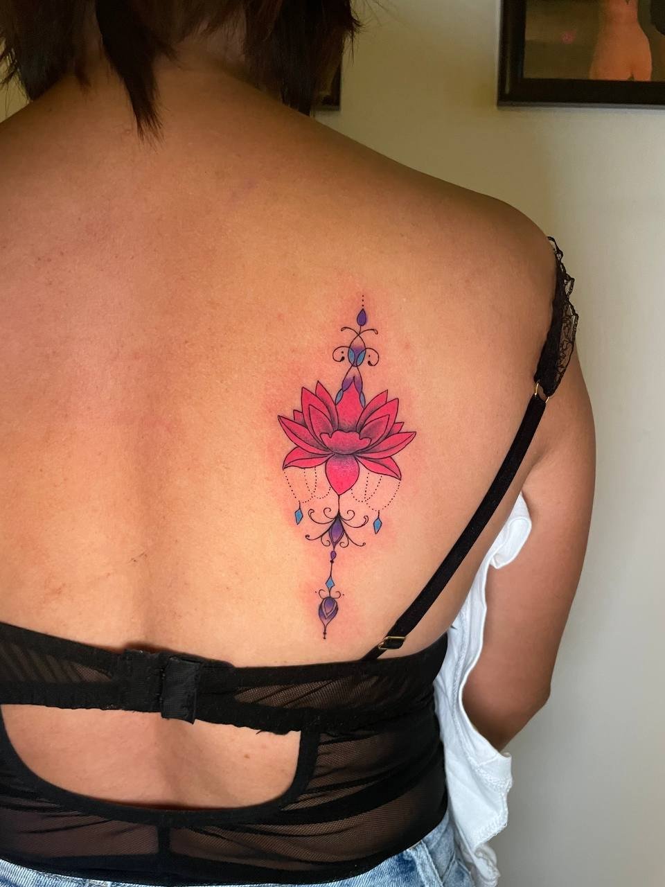 A pink lotus with purple and blue ornamental details on the upper back. Tattoo by Edboi