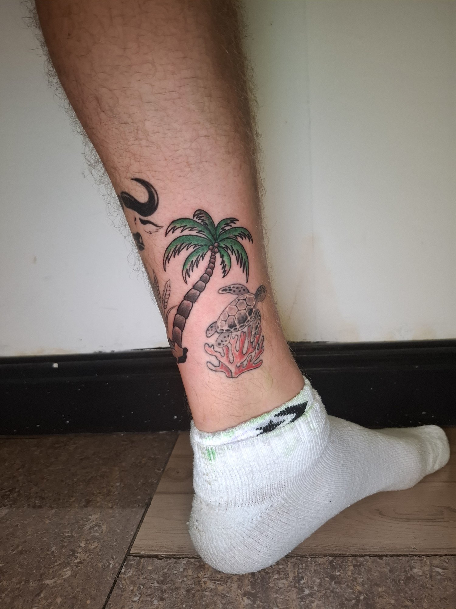 A green palm tree beside a shaded sea turtle and red coral above the ankle. Tattoo by Edboi