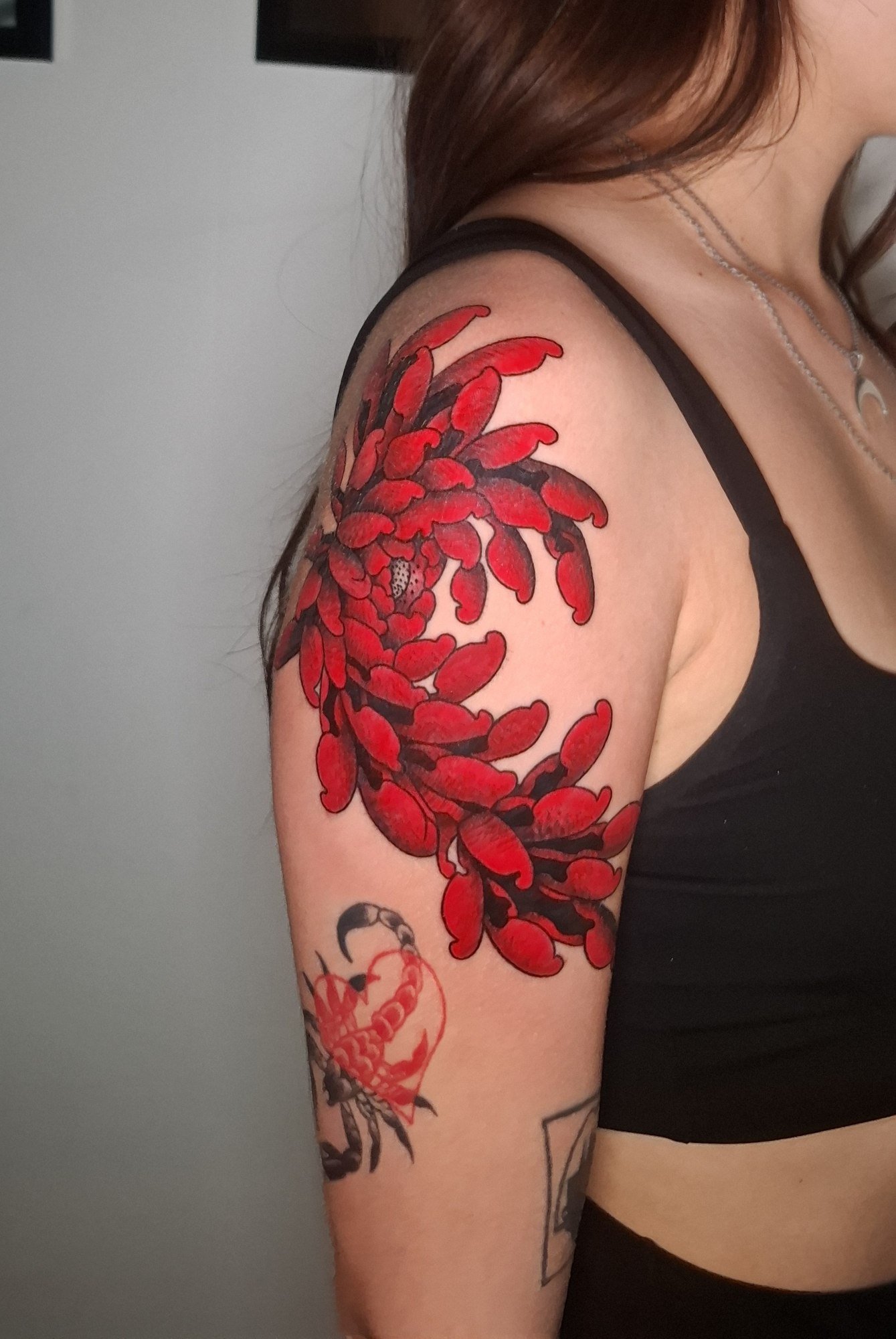 Red chrysanthemums with bold black shading across the shoulder and upper arm. Tattoo by Edboi