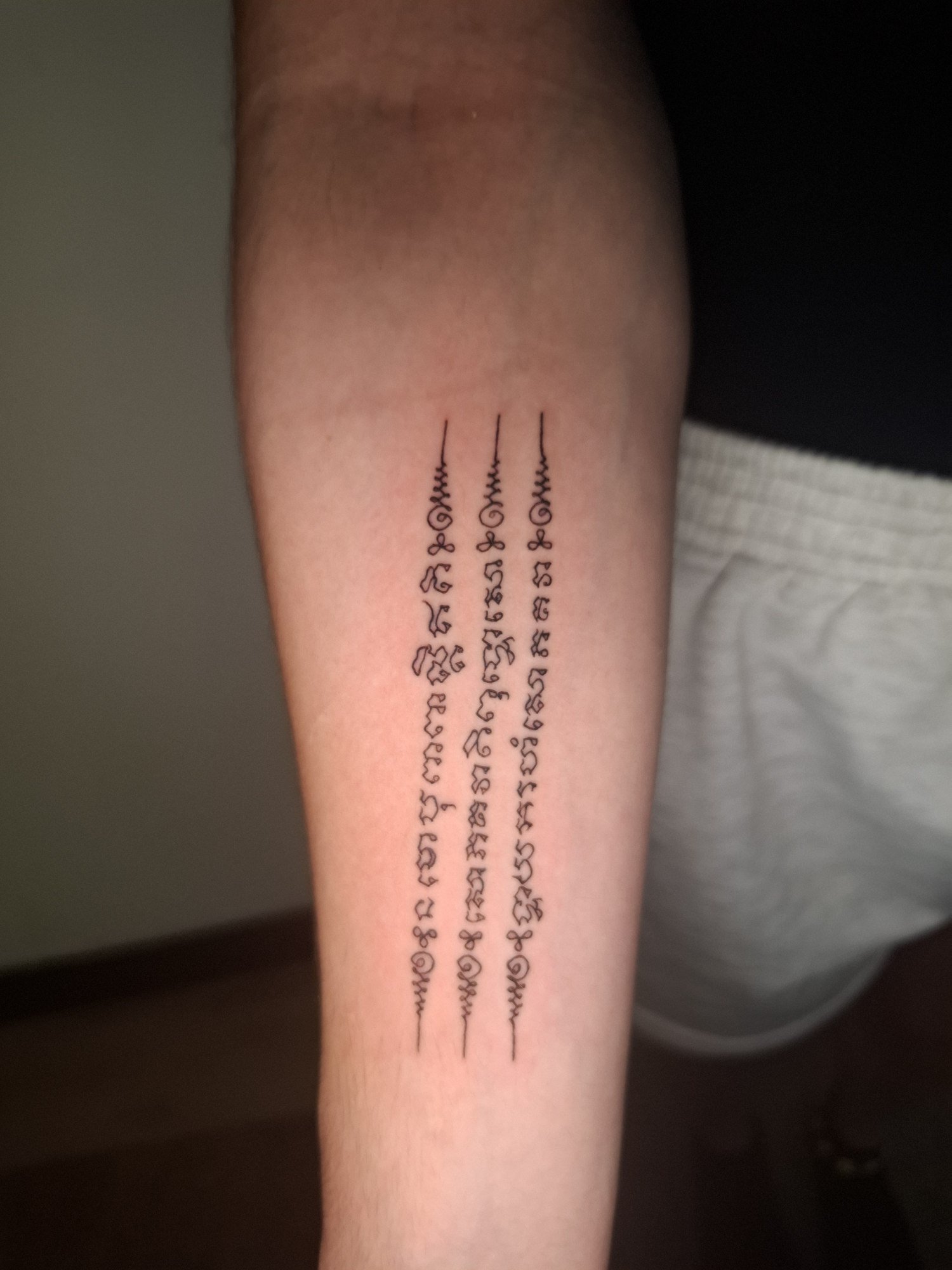 Three vertical columns of fine ornamental script with looping symbols and long pointed ends on the forearm. Tattoo by Edboi