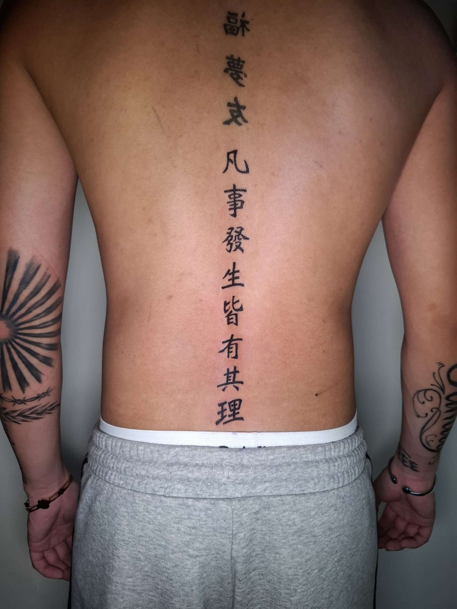 A long column of black characters down the centre of the back. Tattoo by Edboi