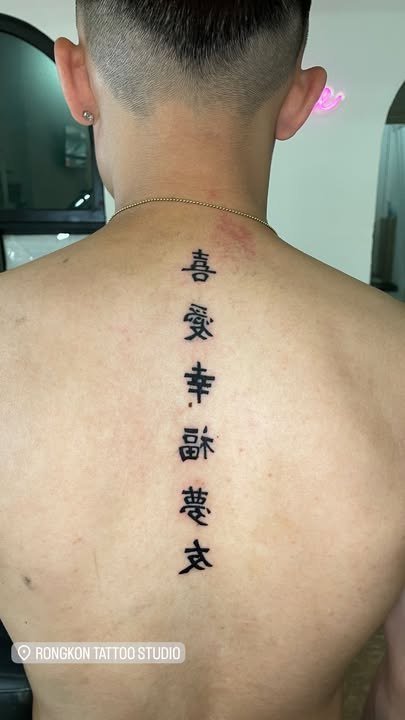 Six bold black characters arranged vertically on the upper back. Tattoo by Edboi