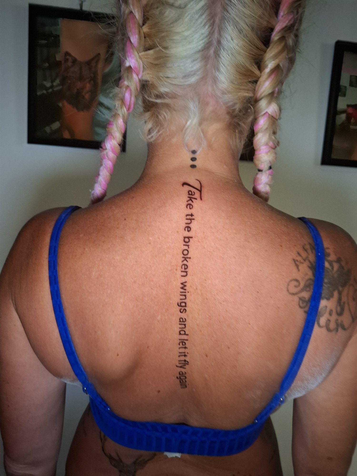 A sentence arranged vertically down the spine beneath three small dots. Tattoo by Edboi